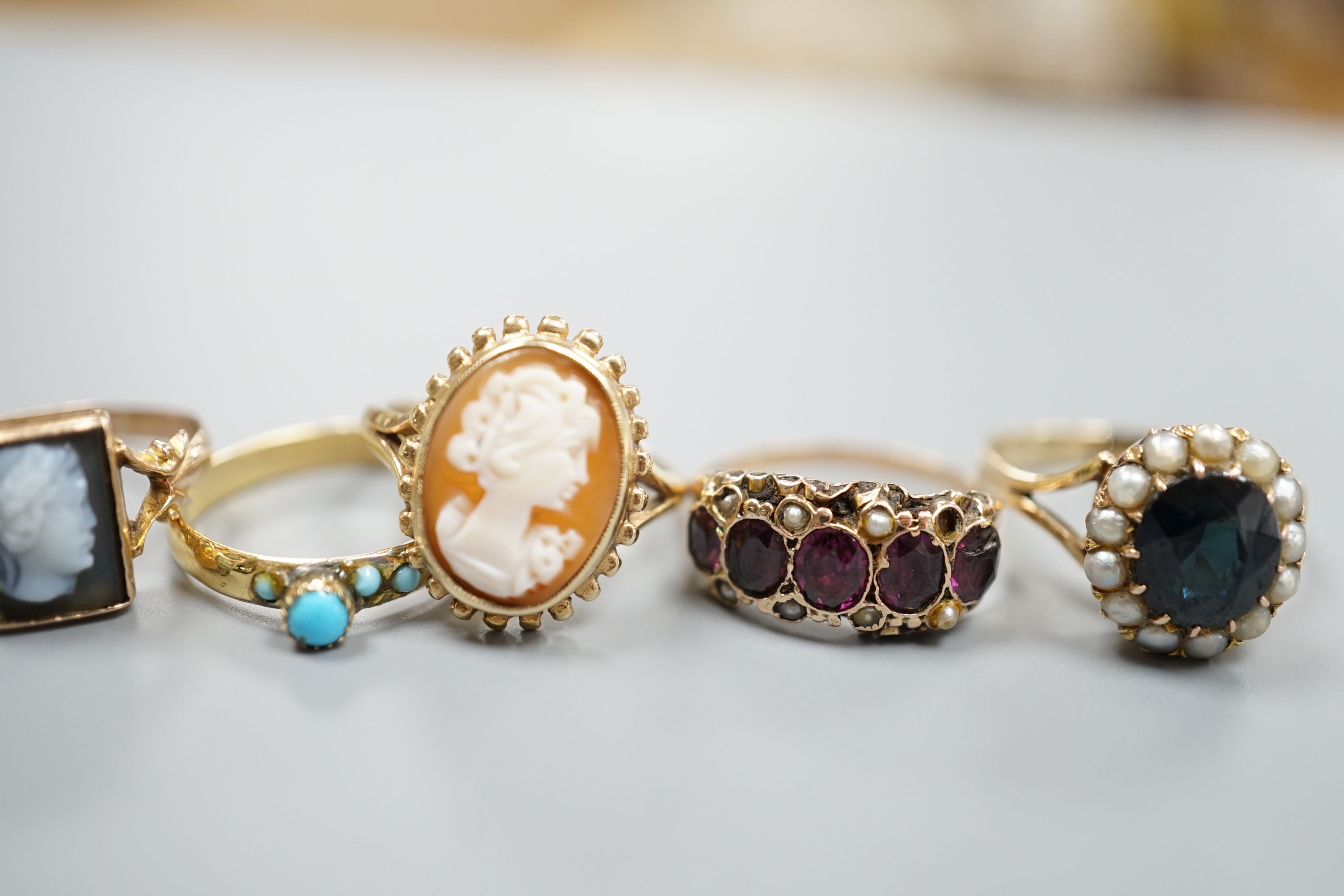 A Victorian yellow metal, garnet and seed pearl half hoop ring(a.f.) and a yellow metal and turquoise set ring, gross 3 grams and three later 9ct gold and gem set rings including two cameo, gross 8.5 grams.